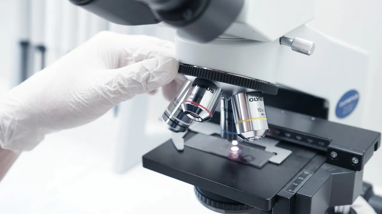 A person in white gloves looking through a microscope
