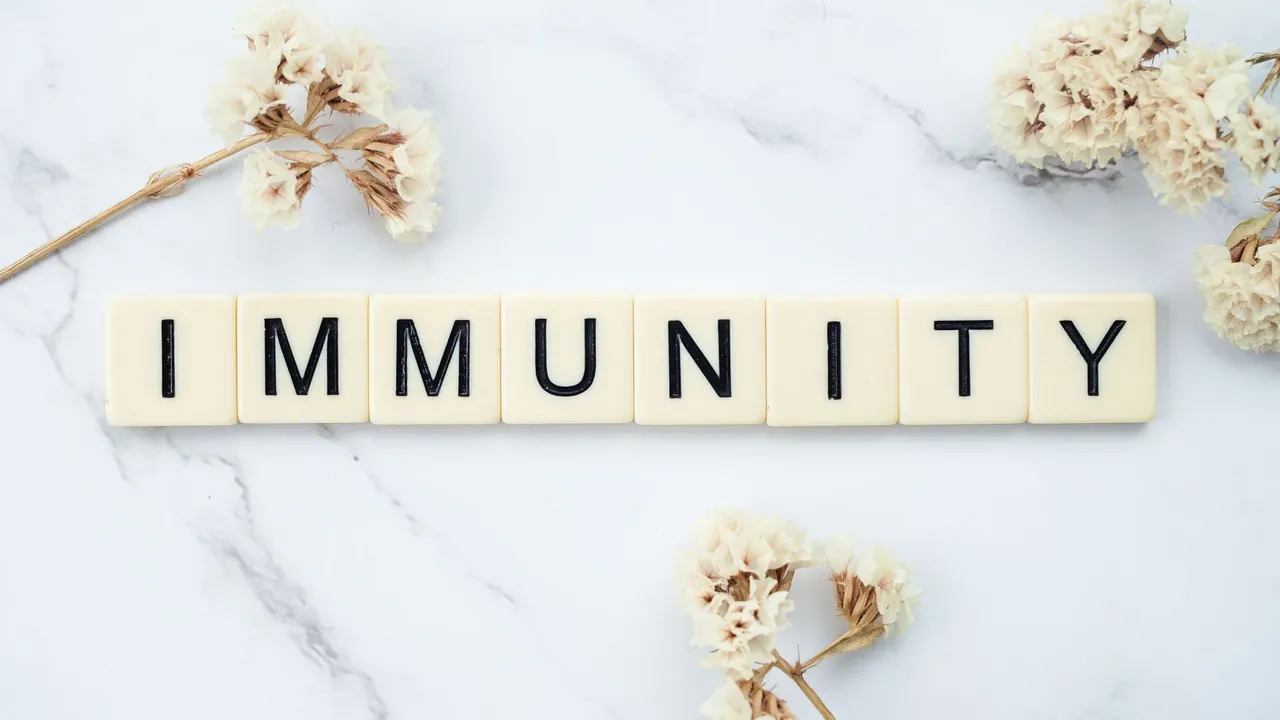 Elegantly arranged scrabble tiles spelling 'immunity' on a marble background with white flowers.