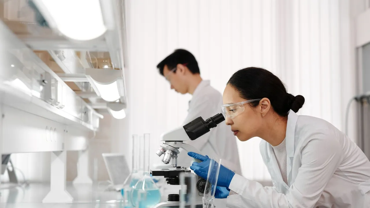 Two scientists in a lab examining samples with a microscope. Focus on scientific research and discovery.