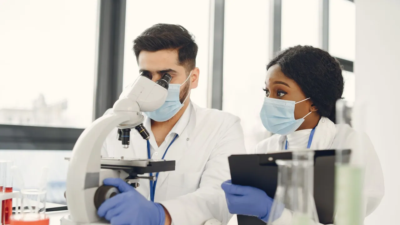 Researchers using a microscope and taking notes in a modern lab.