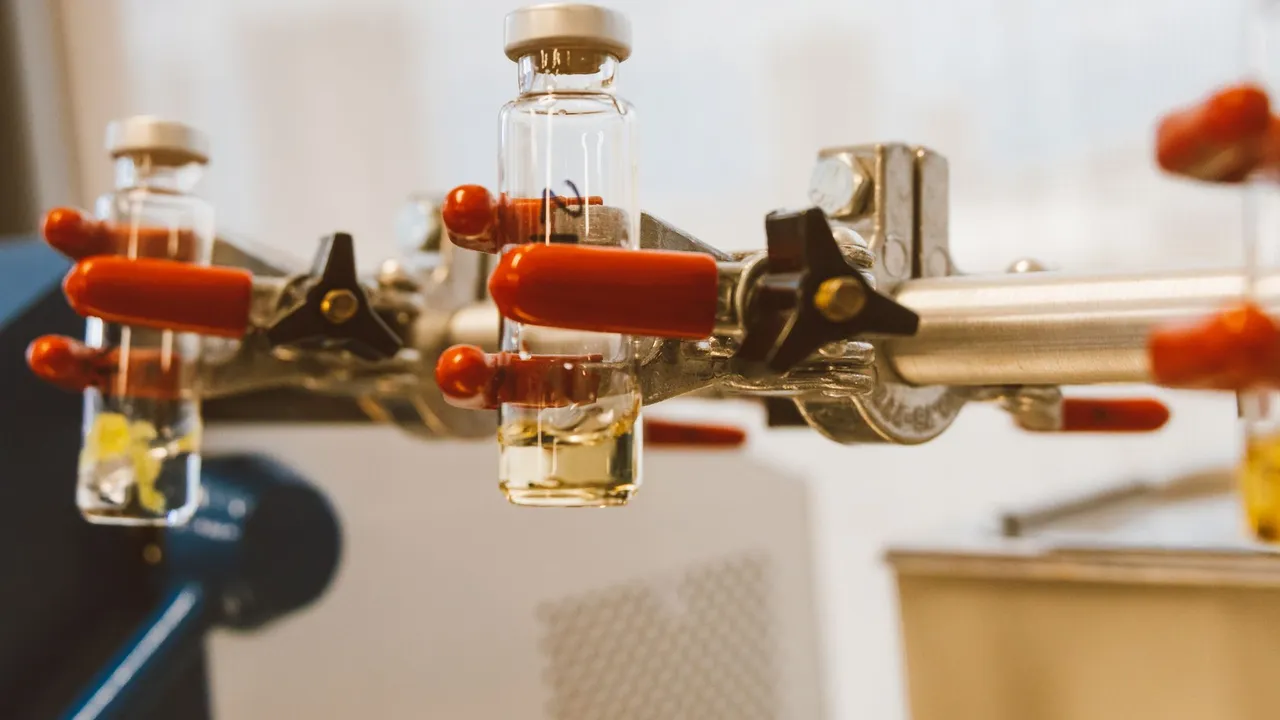 Detailed view of laboratory glass vials held by a clamp with red handles, ideal for science stock images.