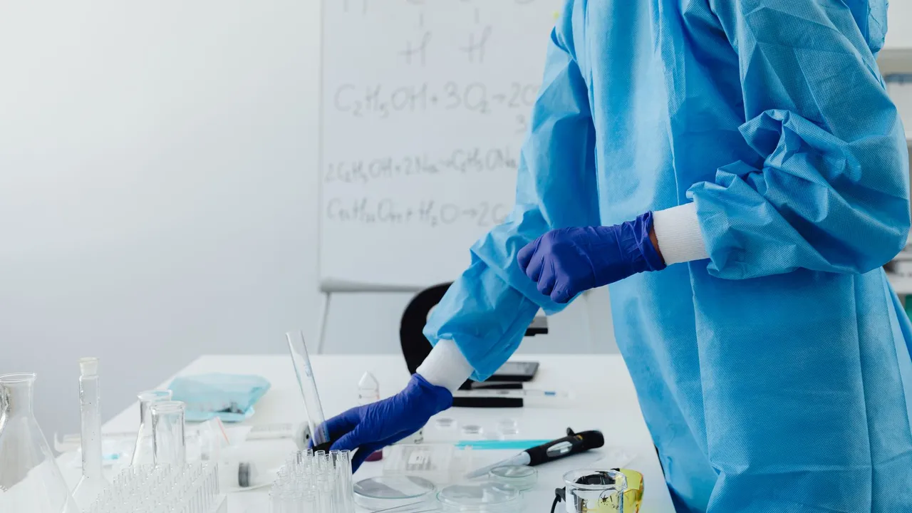 Scientist in protective clothing working in lab with chemical formulas on whiteboard.