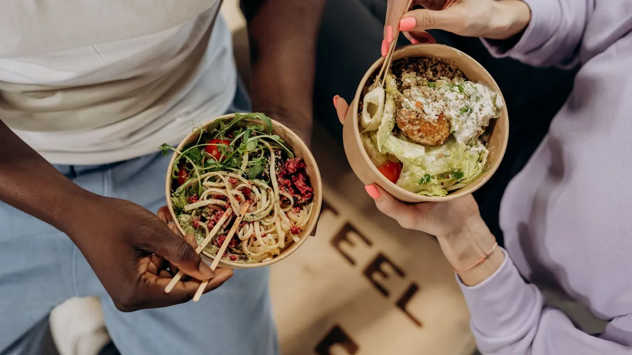 Two people holding bowls filled with salad and pasta, emphasizing healthy lifestyle choices.