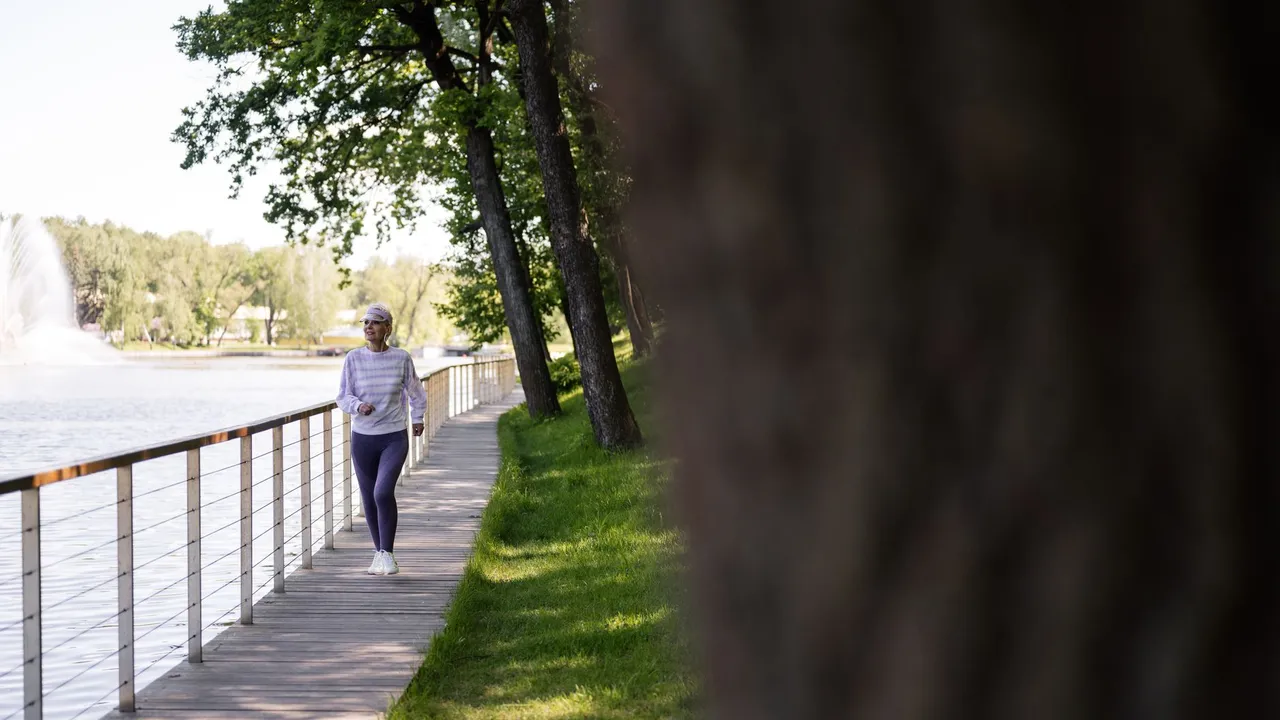 A senior woman enjoys a healthy walk on a lakeside boardwalk on a sunny day.