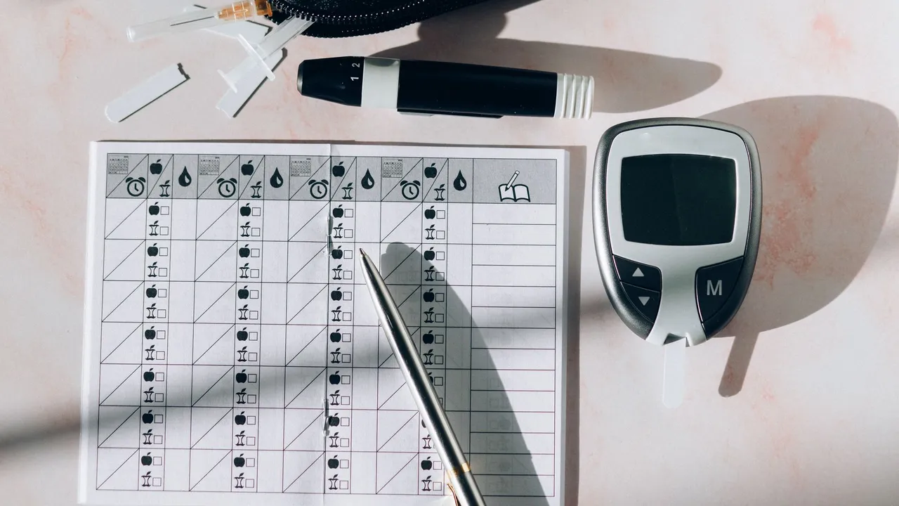 Close-up of a diabetes monitoring kit with glucometer, pen, and test strips on a table.