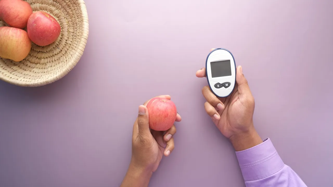 Hands holding apple and glucometer on purple surface, symbolizing health balance.